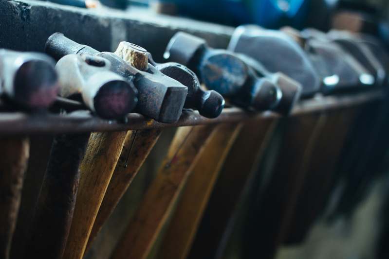 Close-up of assorted hammers including claw, ball-peen, and framing hammers on a wooden workbench